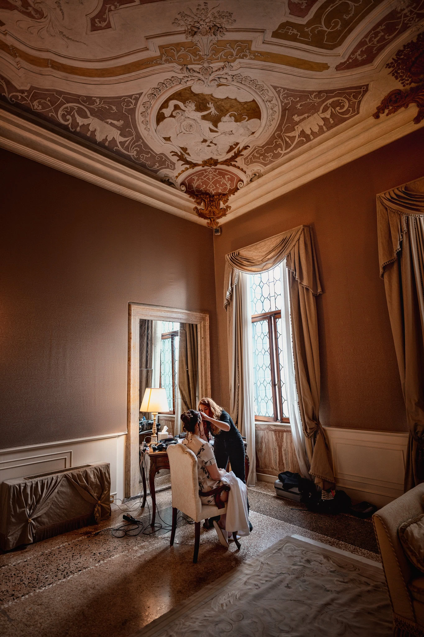 A couple sitting in an elegant room at Ca’ Sagredo Palace, with ornate ceiling details and.