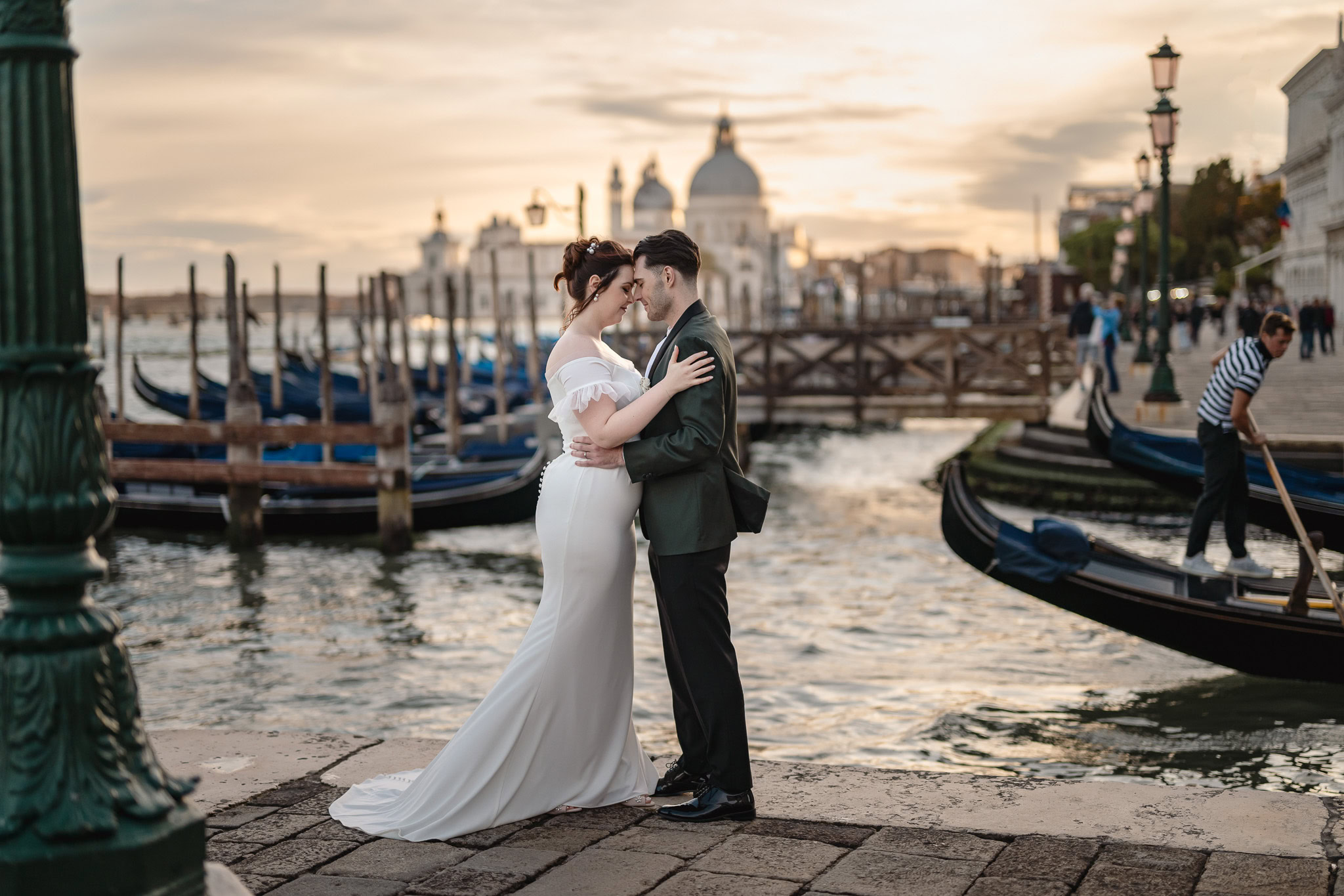 Couple embracing near Ca’ Sagredo Palace with gondolas in Venice at sunset.