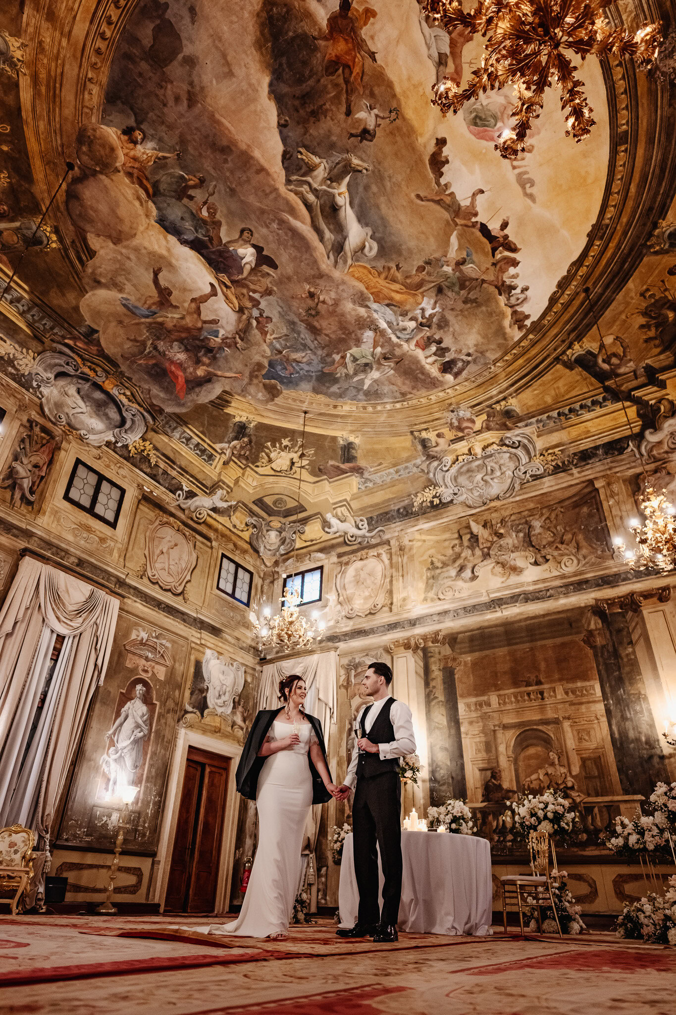 Elegant couple holding hands inside Ca’ Sagredo Palace with ornate ceiling artwork.