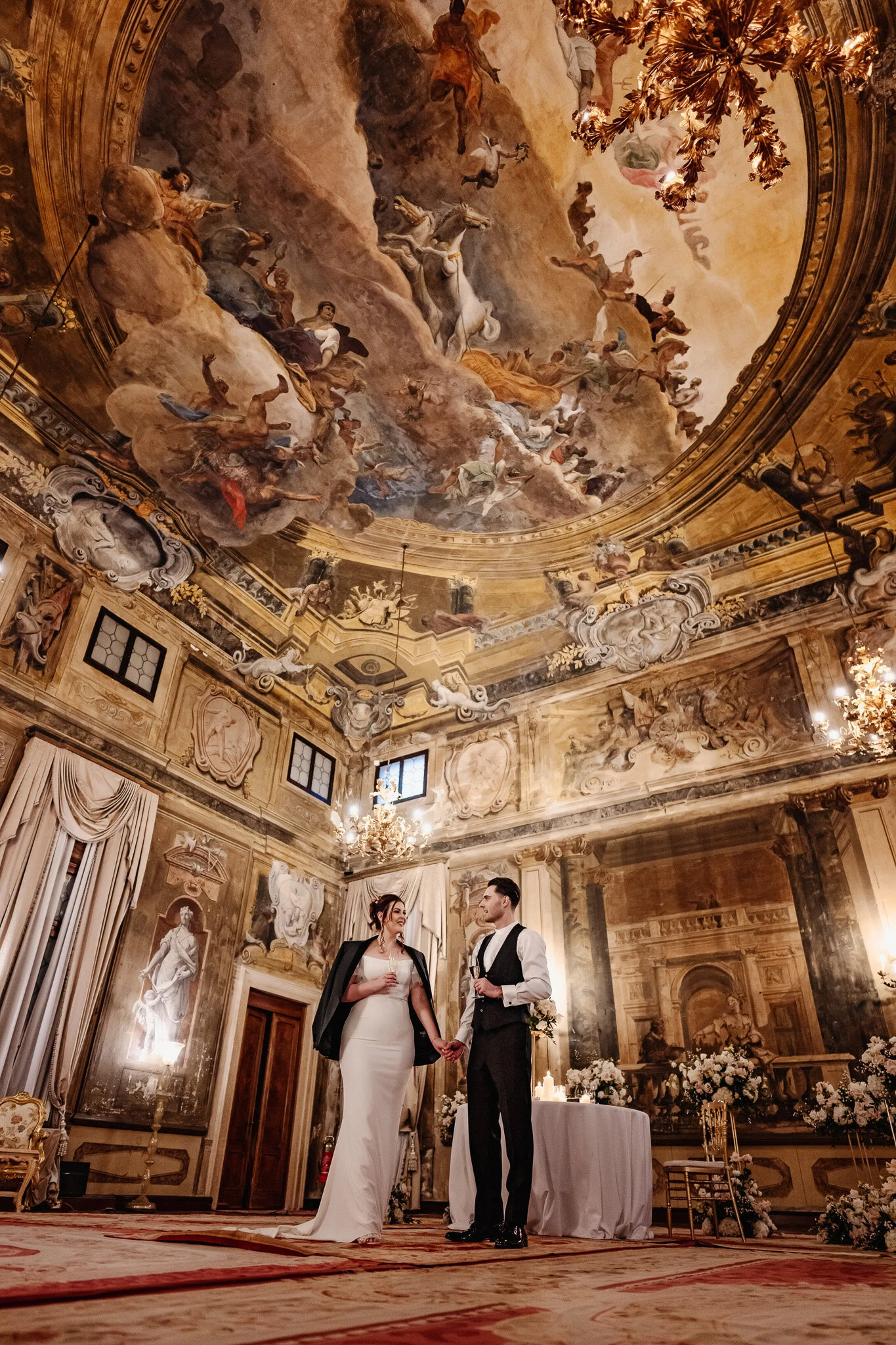 Elegant couple holding hands inside Ca’ Sagredo Palace with ornate ceiling artwork.