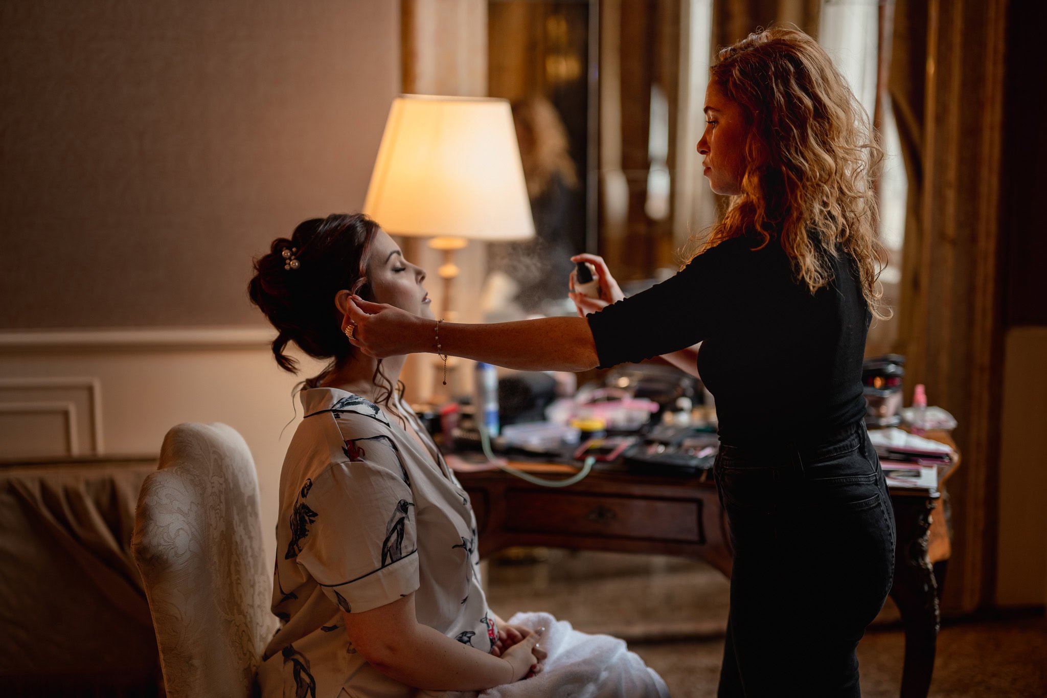 A woman applying makeup to another woman seated in a luxurious room at Ca’ Sagredo Palace.
