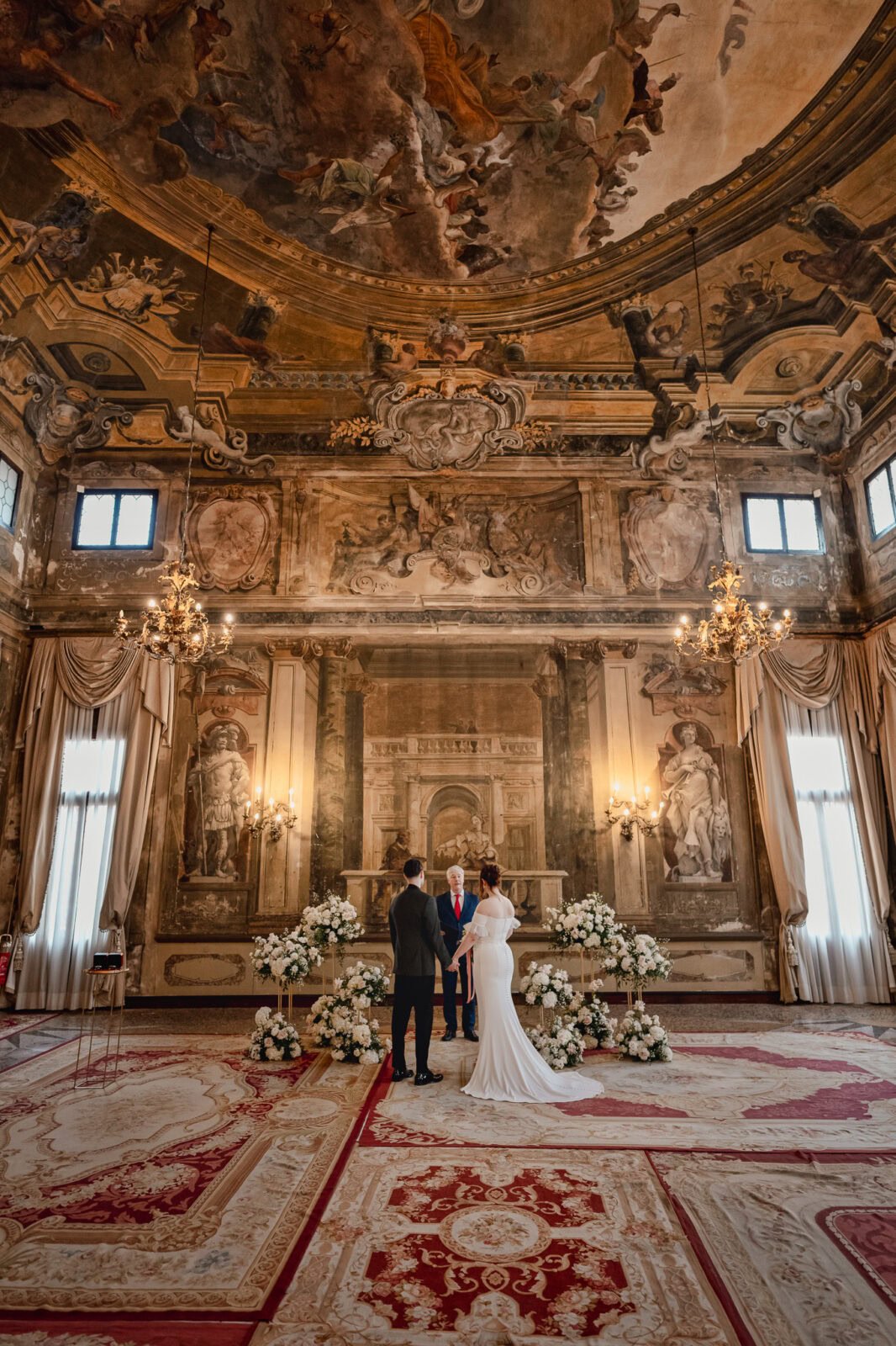 Elegant couple in a grand Venetian palace interior with ornate frescoes and chandeliers.