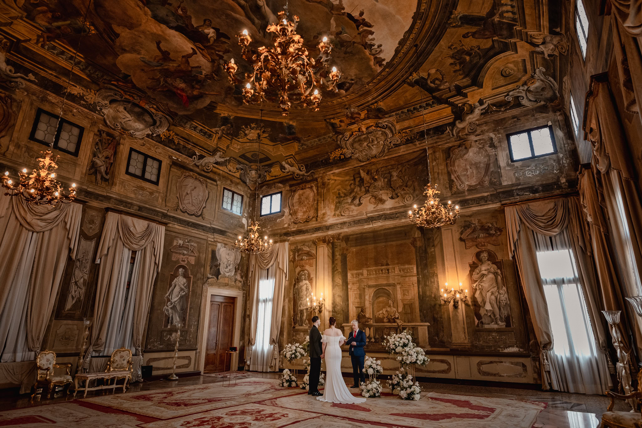 Elegant couple standing inside Ca’ Sagredo Palace with ornate ceiling and classical decor.