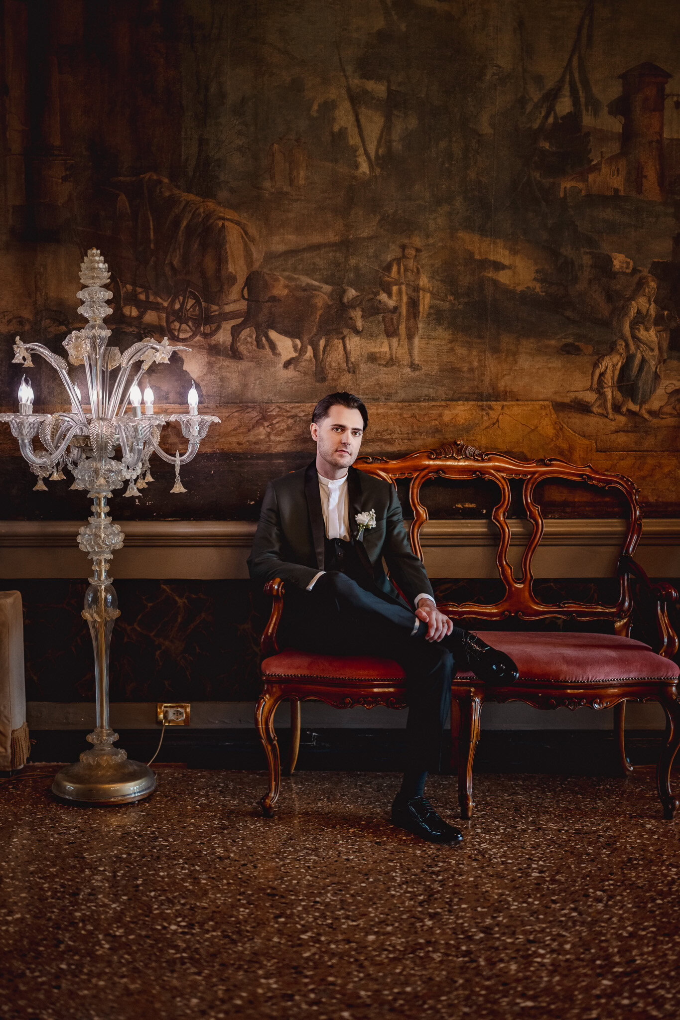 A man sitting on a vintage red and gold bench in a luxurious room at Ca’ Sagredo Palace, V.