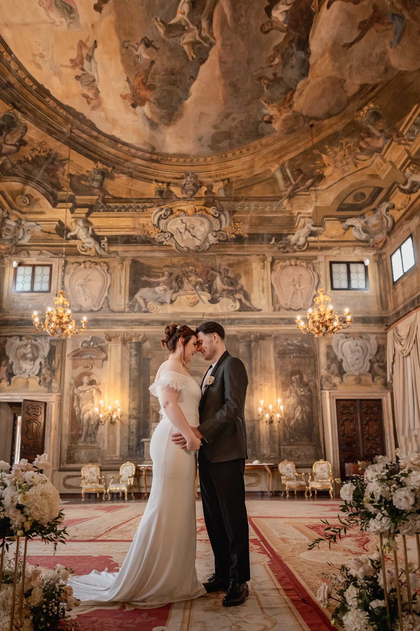 Elegant couple standing inside Ca’ Sagredo Palace with ornate ceiling and chandeliers in t.