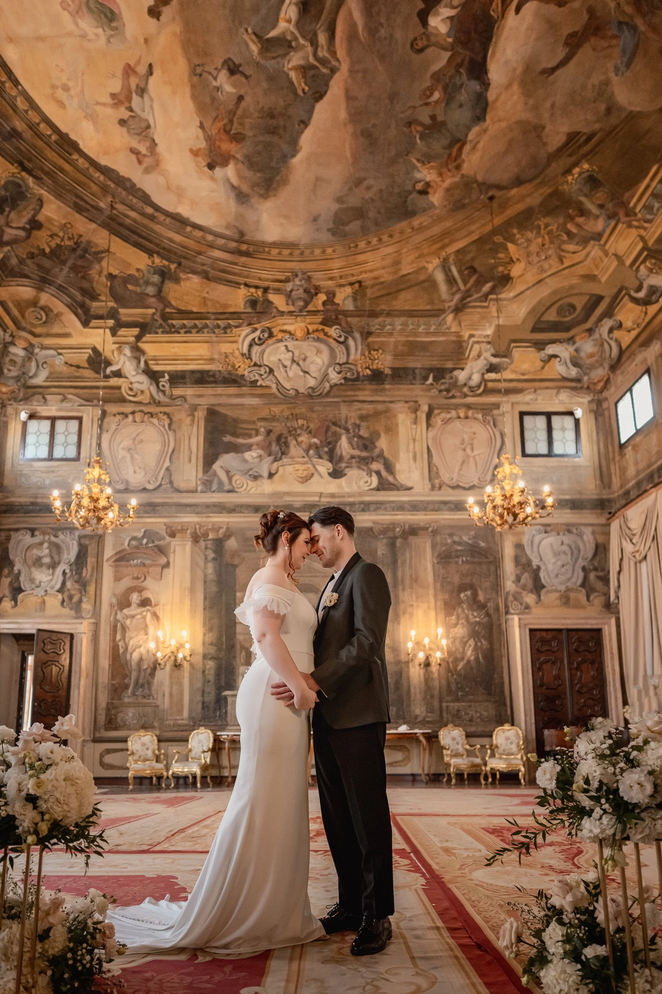 Elegant couple standing inside Ca’ Sagredo Palace with ornate ceiling and chandeliers in t.