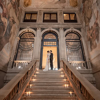 Elegant couple standing on grand staircase inside Ca’ Sagredo Palace, Venice, with ornate.