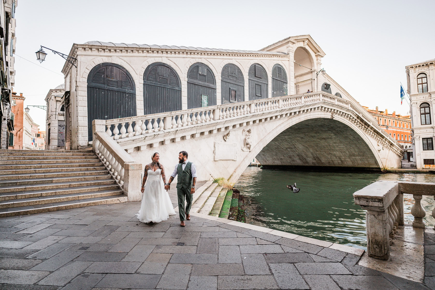 Romantic couple walking hand-in-hand near Rialto Bridge at dawn in Venice, serene and inti.
