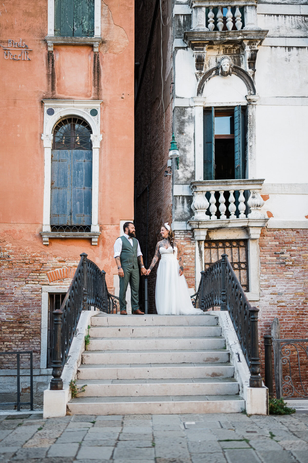 A woman and man holding hands on a staircase in Venice, surrounded by colorful historic bu.