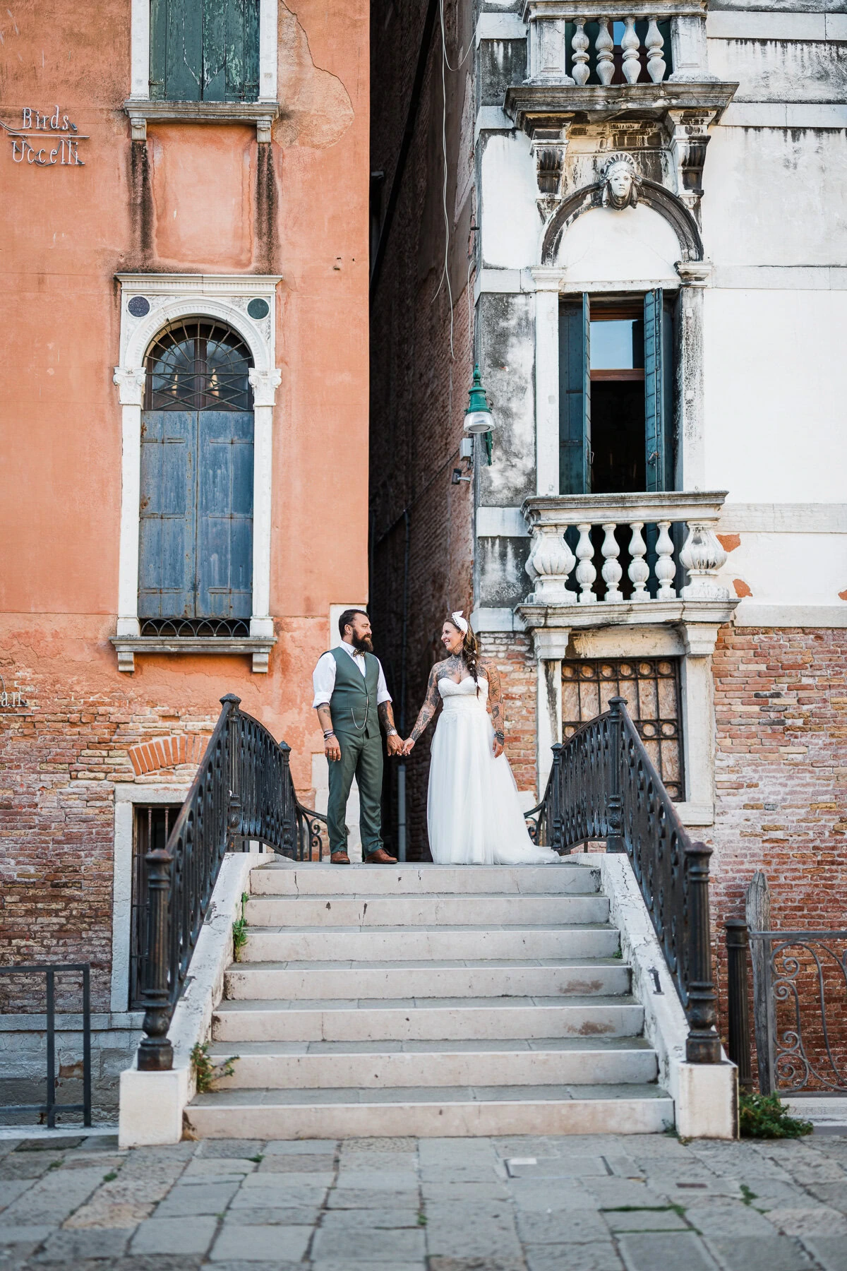 A woman and man holding hands on a staircase in Venice, surrounded by colorful historic bu.