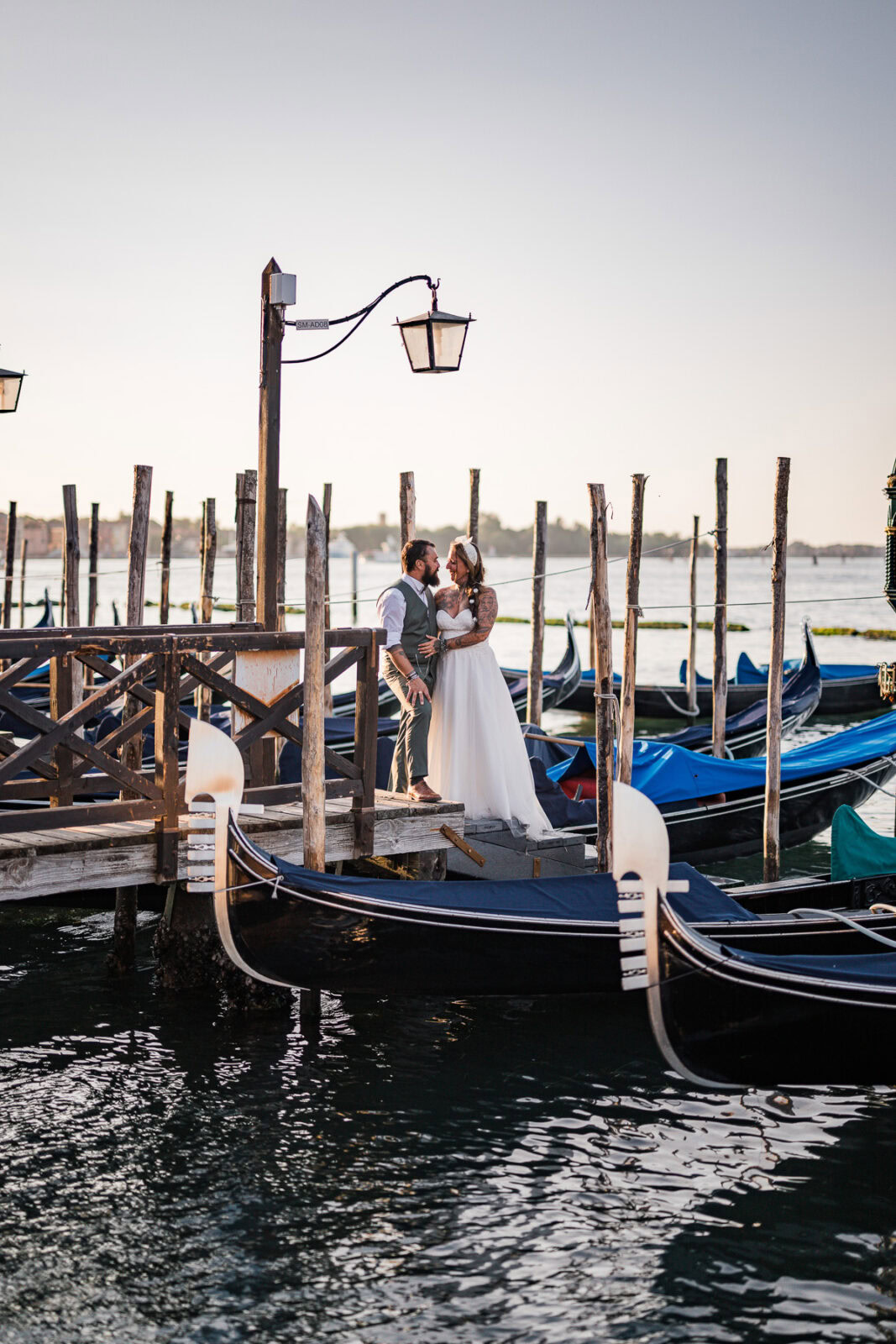 Romantic couple on a Venice dock at sunrise, boats and calm water in the background.