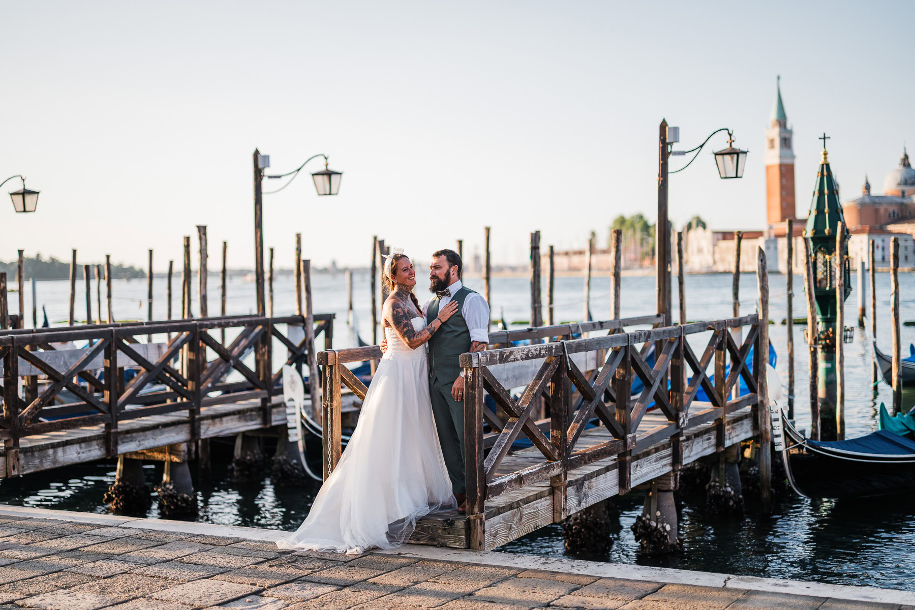 Romantic newlyweds embrace on a Venice dock at sunrise, with calm waters and historic arch.