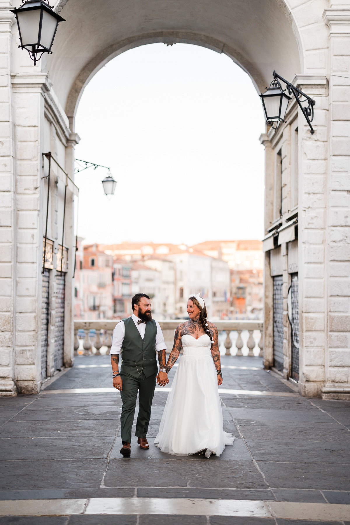 Romantic couple walking through Venice archway at dawn, soft light, intimate moment, early.