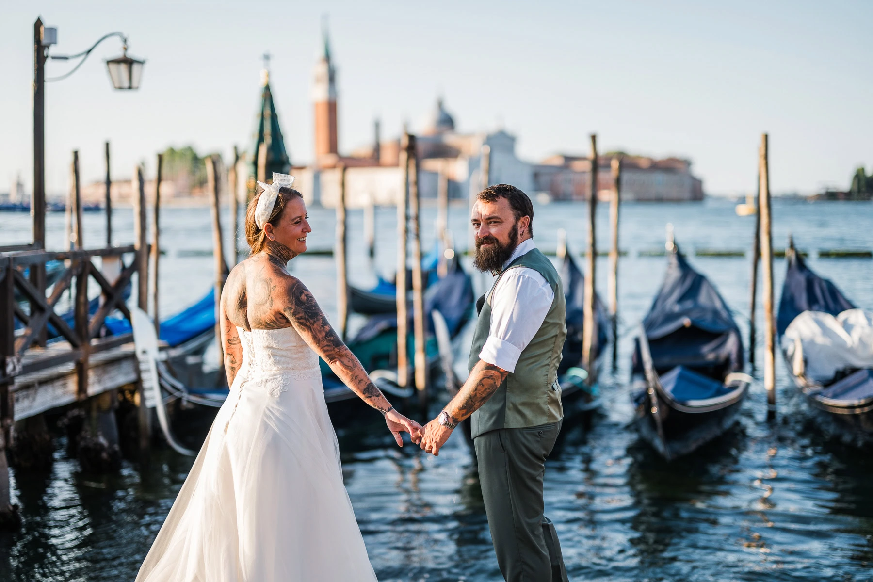 Romantic couple holding hands by Venice canal during early morning light.
