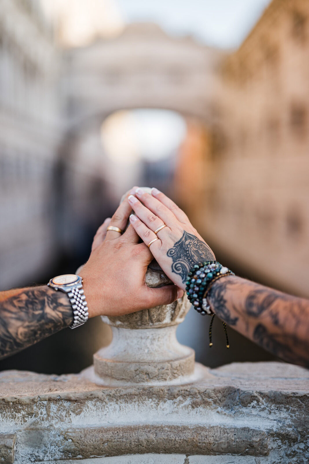 Hands of a couple with wedding rings and tattoos resting on a stone balustrade in Venice a.