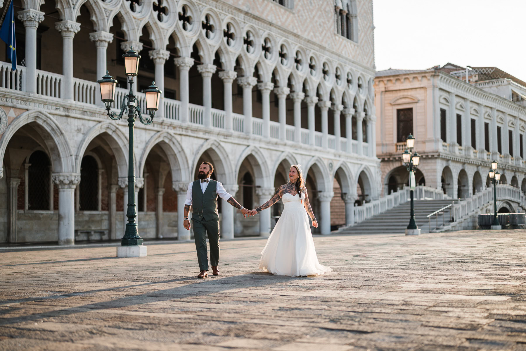 A woman and man holding hands walking through an empty Venice square at dawn, soft light a.