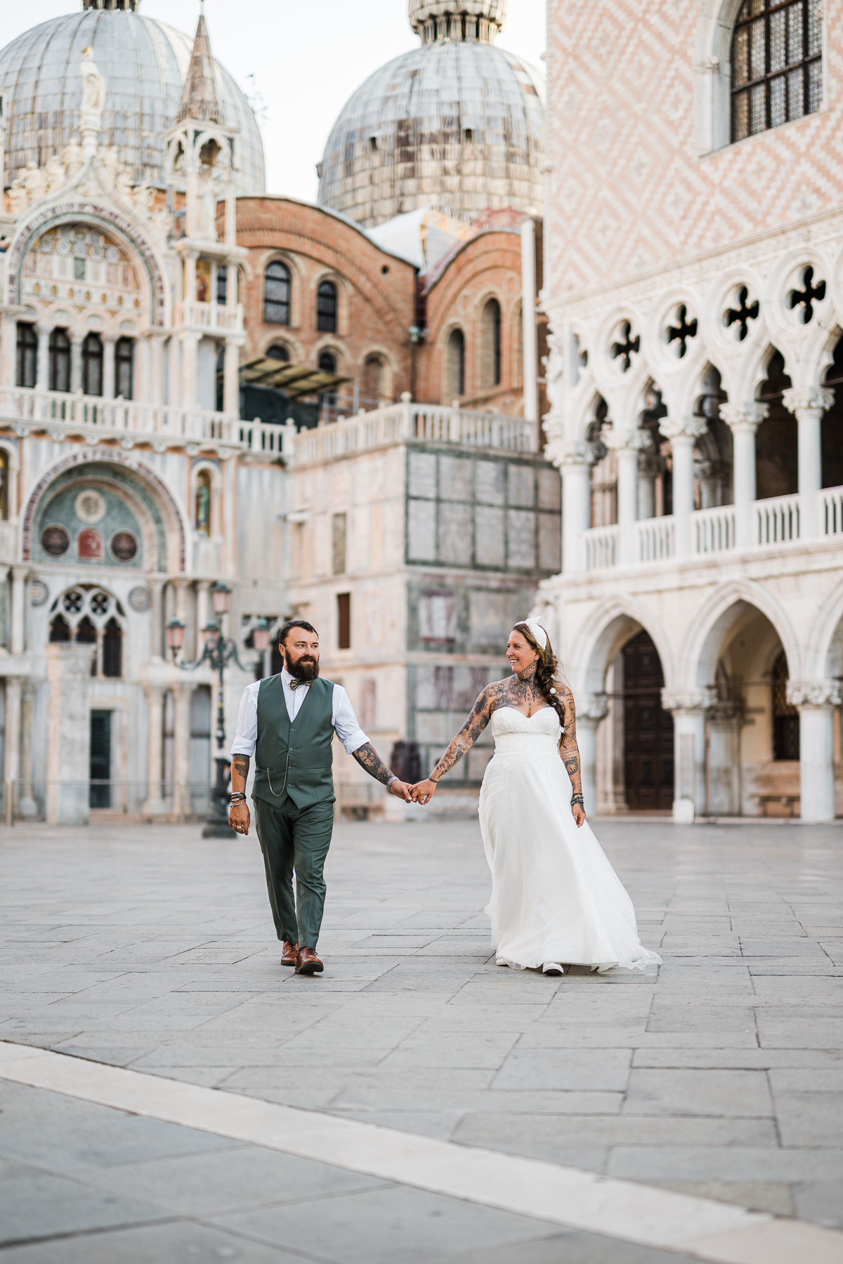 Romantic couple walking hand in hand in Venice's historic square at dawn.
