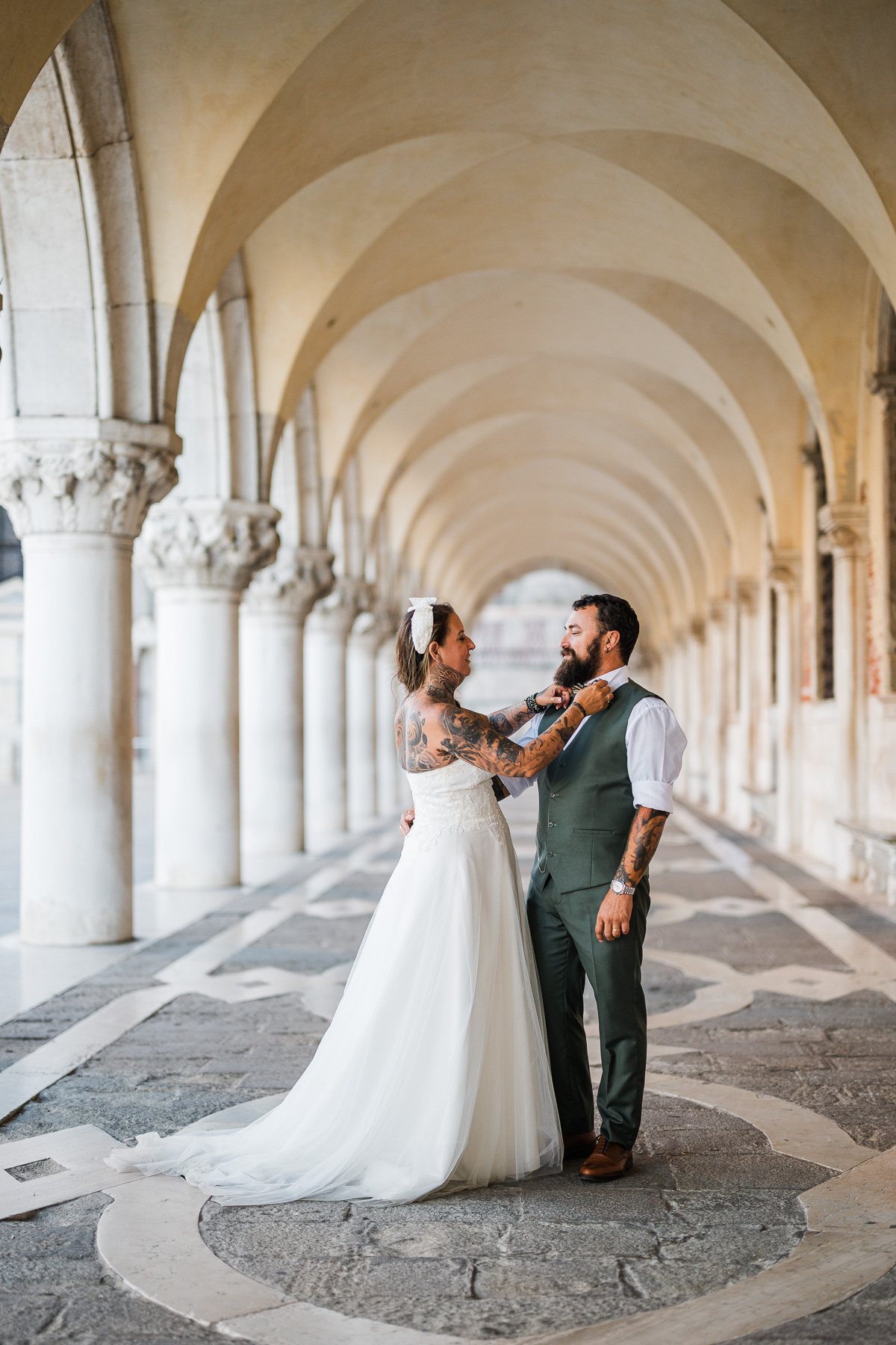 A woman and man in wedding attire sharing a tender moment under historic arches in Venice.