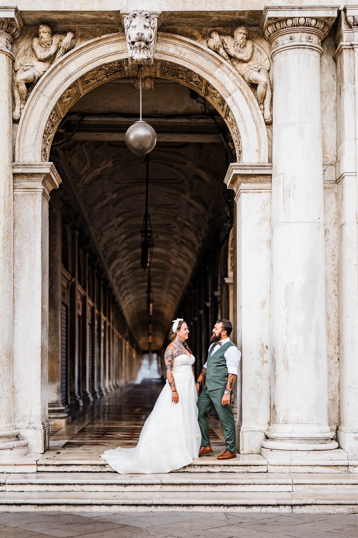 Romantic couple standing under historic archway in Venice during early morning light.