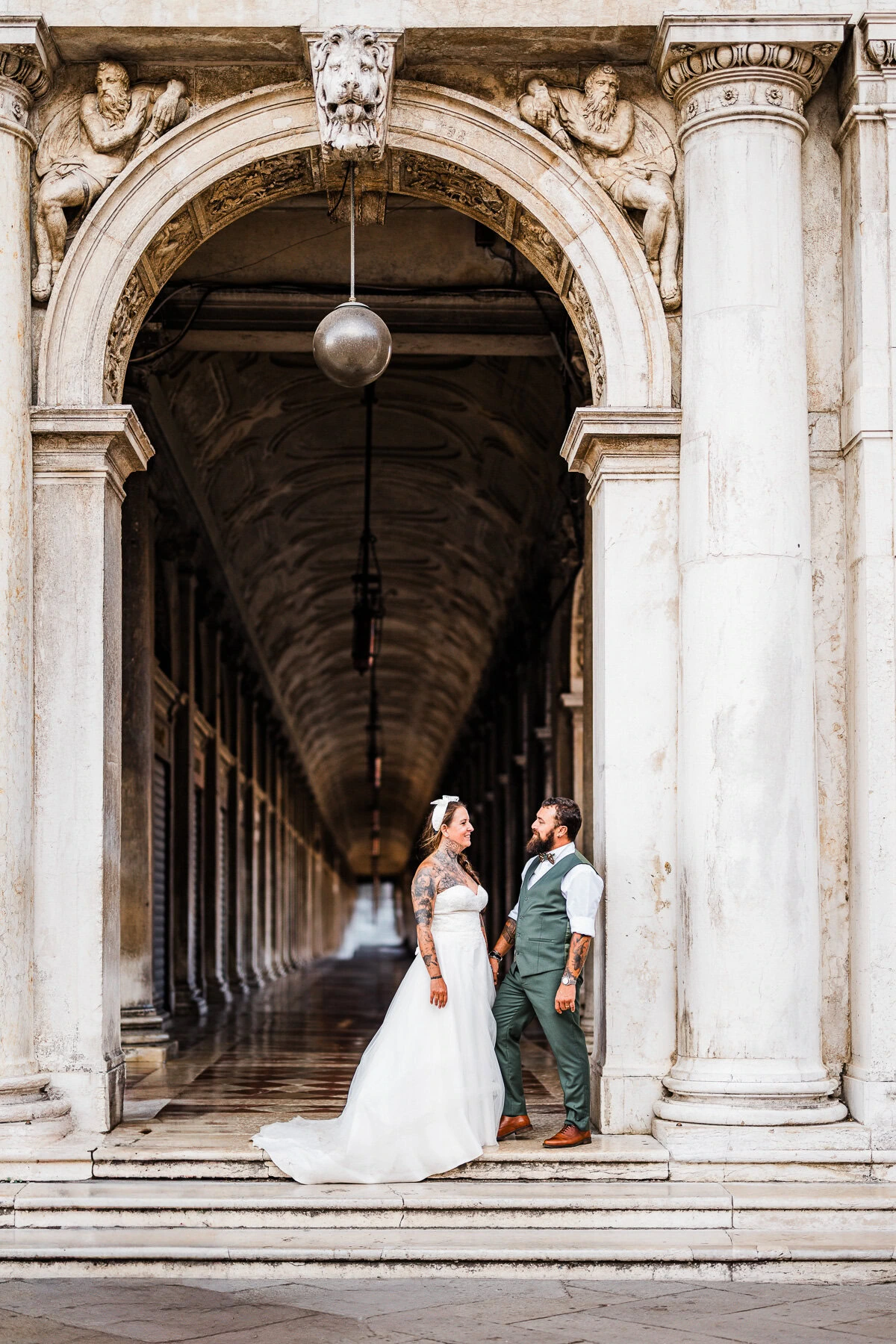 Romantic couple standing under historic archway in Venice during early morning light.
