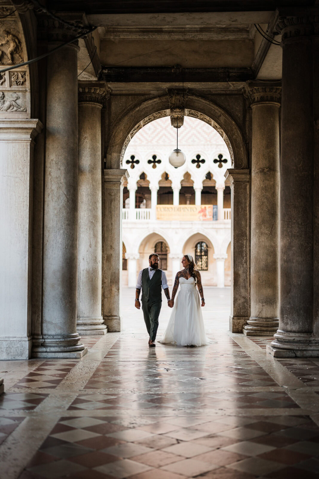 Elegant couple walking hand in hand through historic Venetian architecture at dawn.