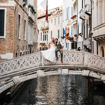 Romantic couple sitting on a small bridge over a canal in Venice during early morning ligh.
