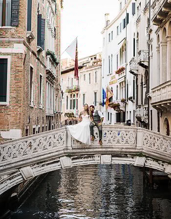Romantic couple sitting on a small bridge over a canal in Venice during early morning ligh.