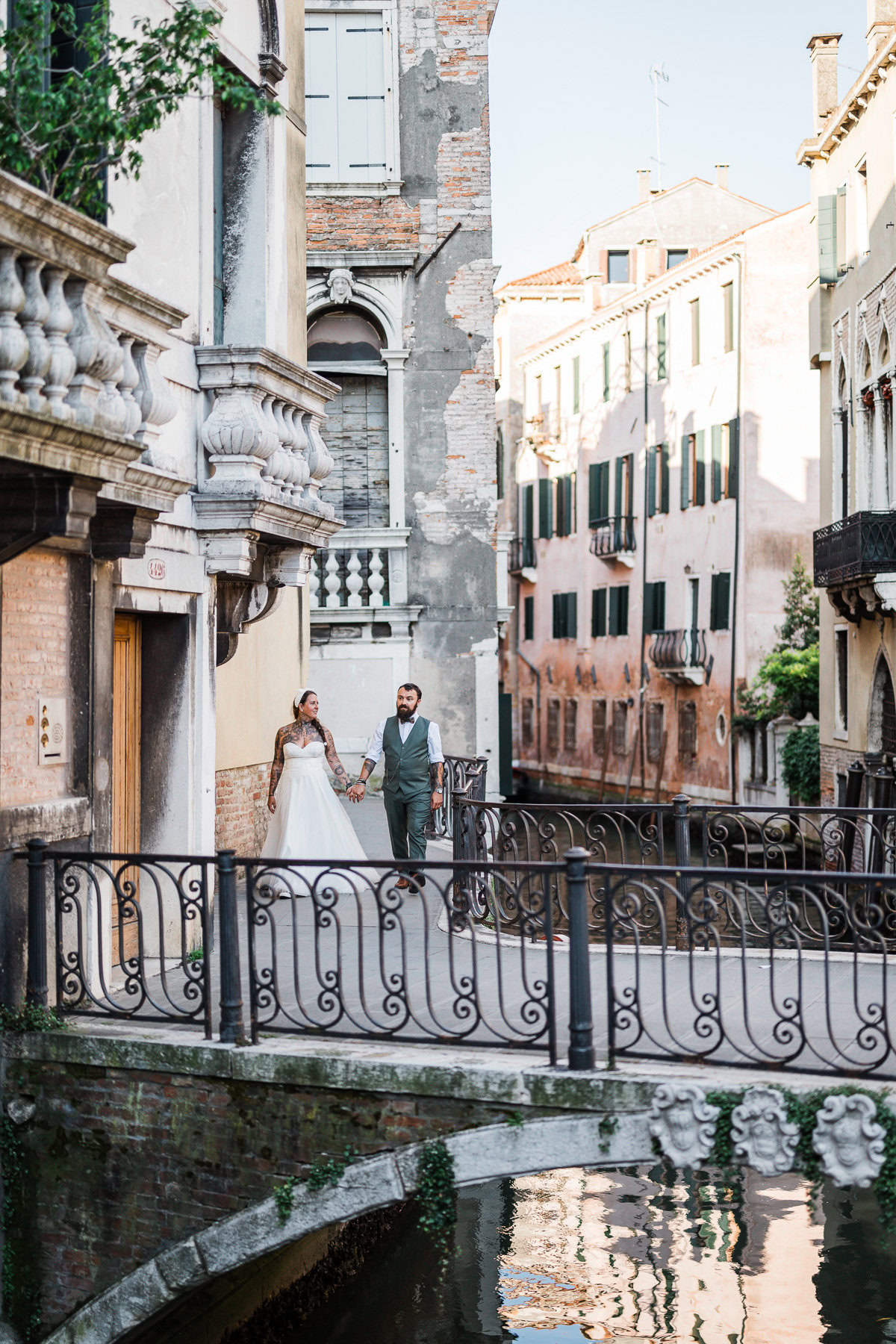 Elegant couple walking hand in hand along a quiet canal in Venice during early morning lig.
