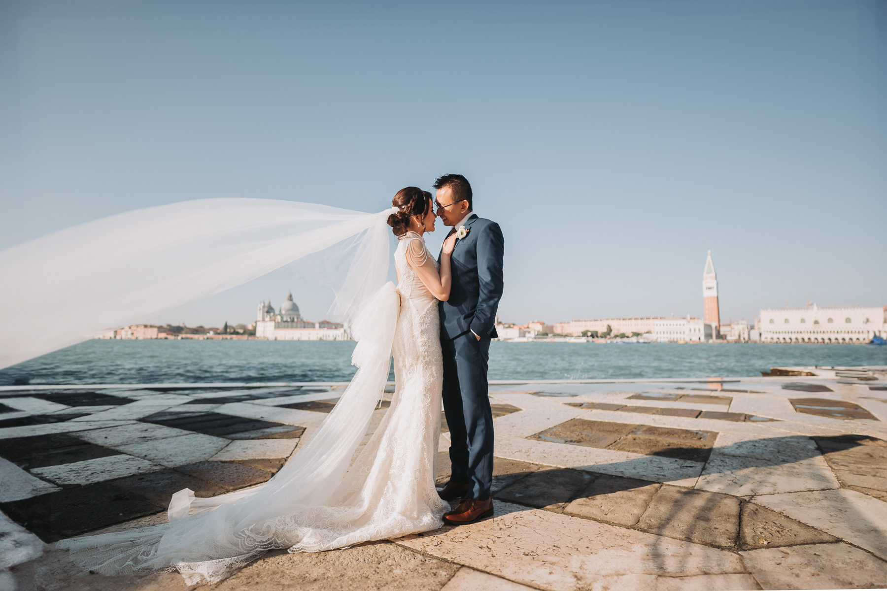 Couple standing by the water at Scuola Grande dei Carmini in Venice, with historic buildin.