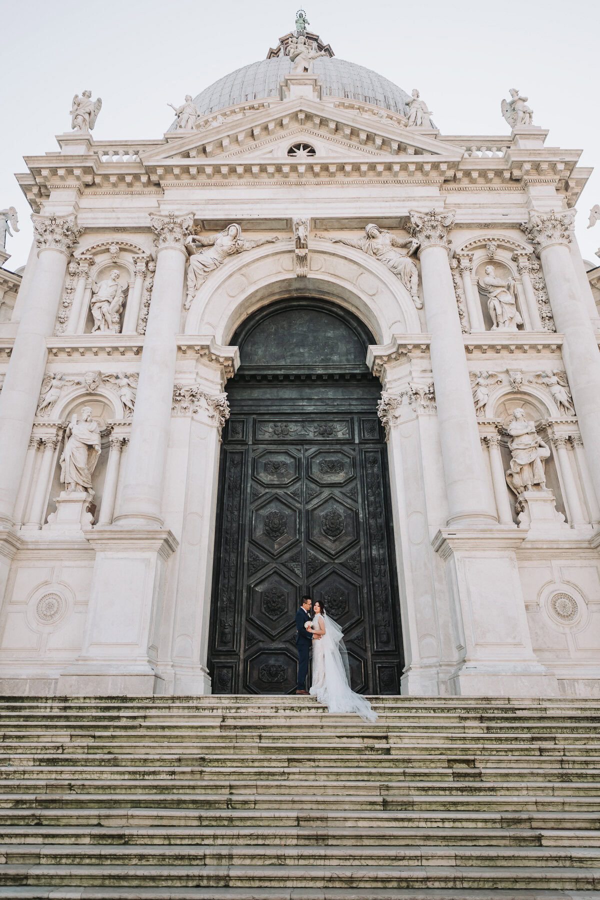 A woman in a white dress standing at the base of the grand entrance of Scuola Grande dei C.