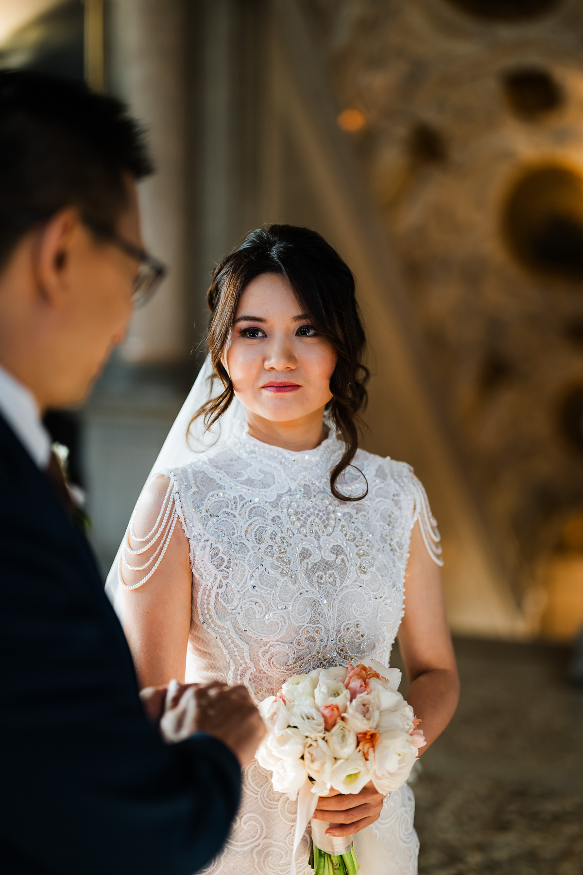 A woman in a lace dress holding a bouquet of white and blush roses at Scuola Grande dei Ca.
