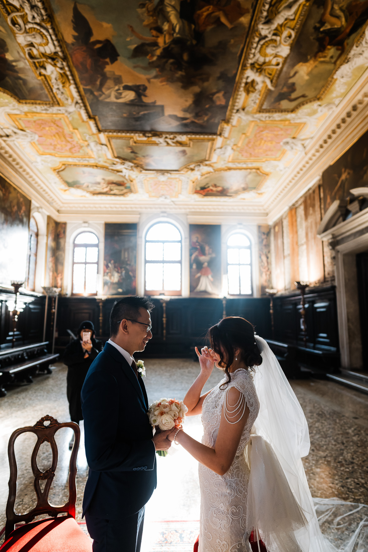 Couple standing inside Scuola Grande dei Carmini with ornate ceiling and large windows in.