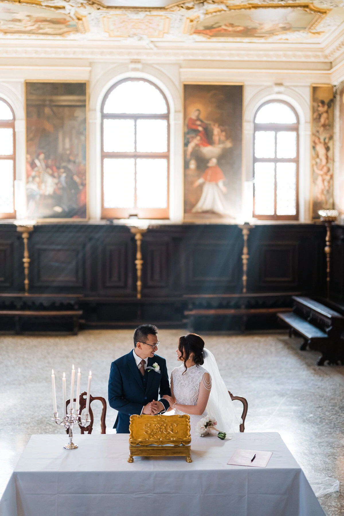 Elegant couple seated at a table with a cake inside Scuola Grande dei Carmini, Venice.
