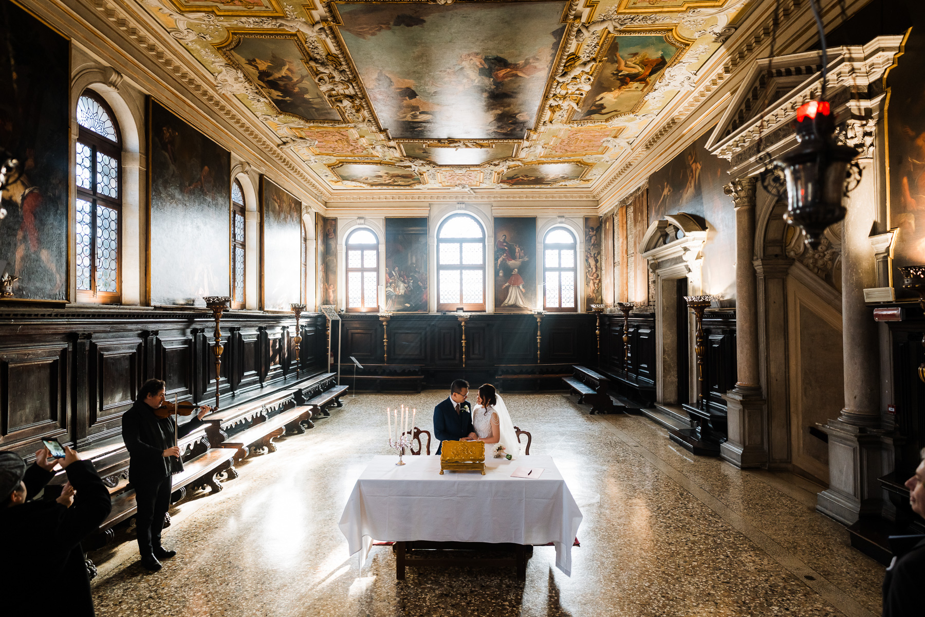 A couple seated at a table inside the ornate Scuola Grande dei Carmini in Venice.