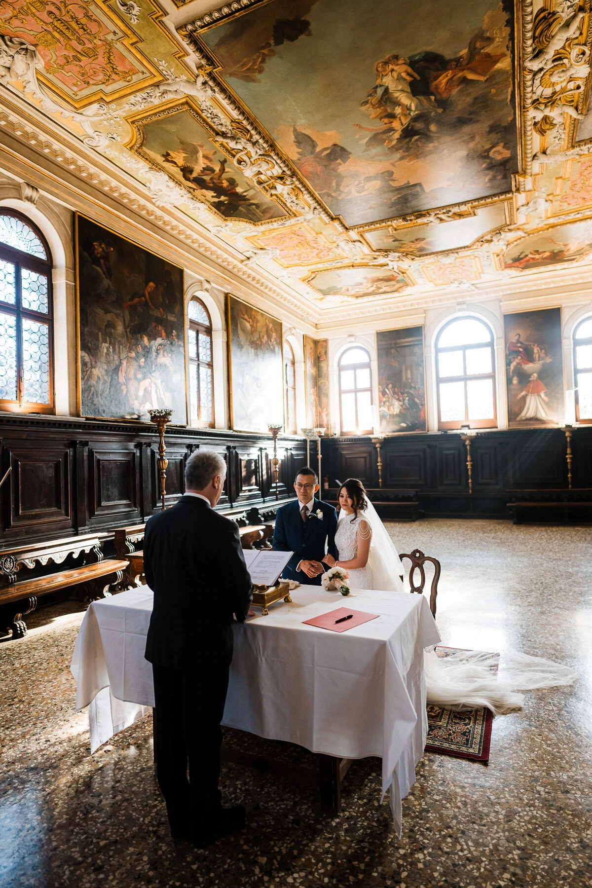Couple at a table inside Scuola Grande dei Carmini with ornate ceiling paintings.