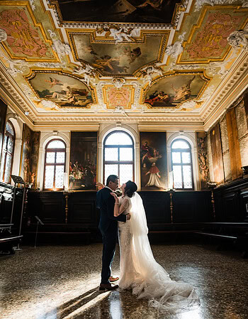 A couple standing close together inside the ornate Scuola Grande dei Carmini with elaborat.