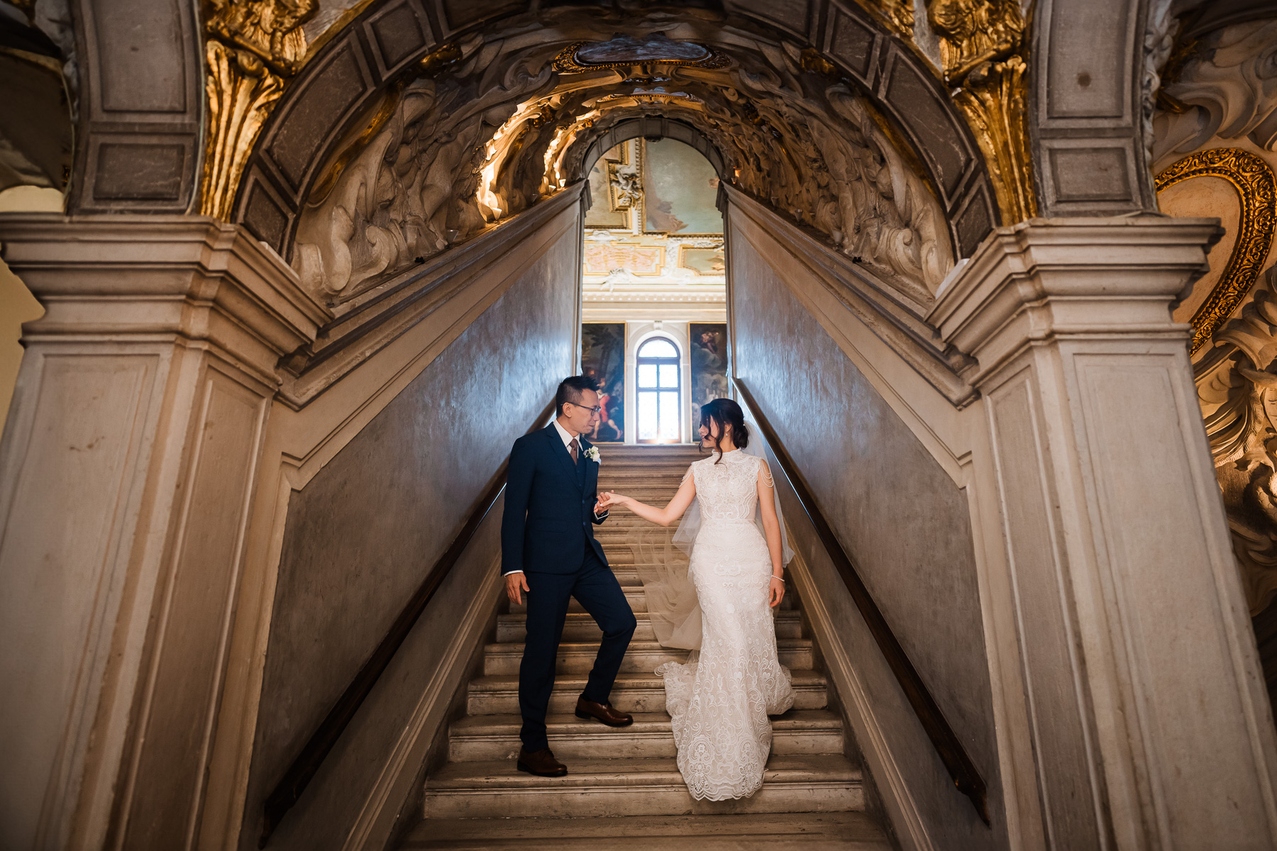 Couple holding hands on staircase inside Scuola Grande dei Carmini in Venice.