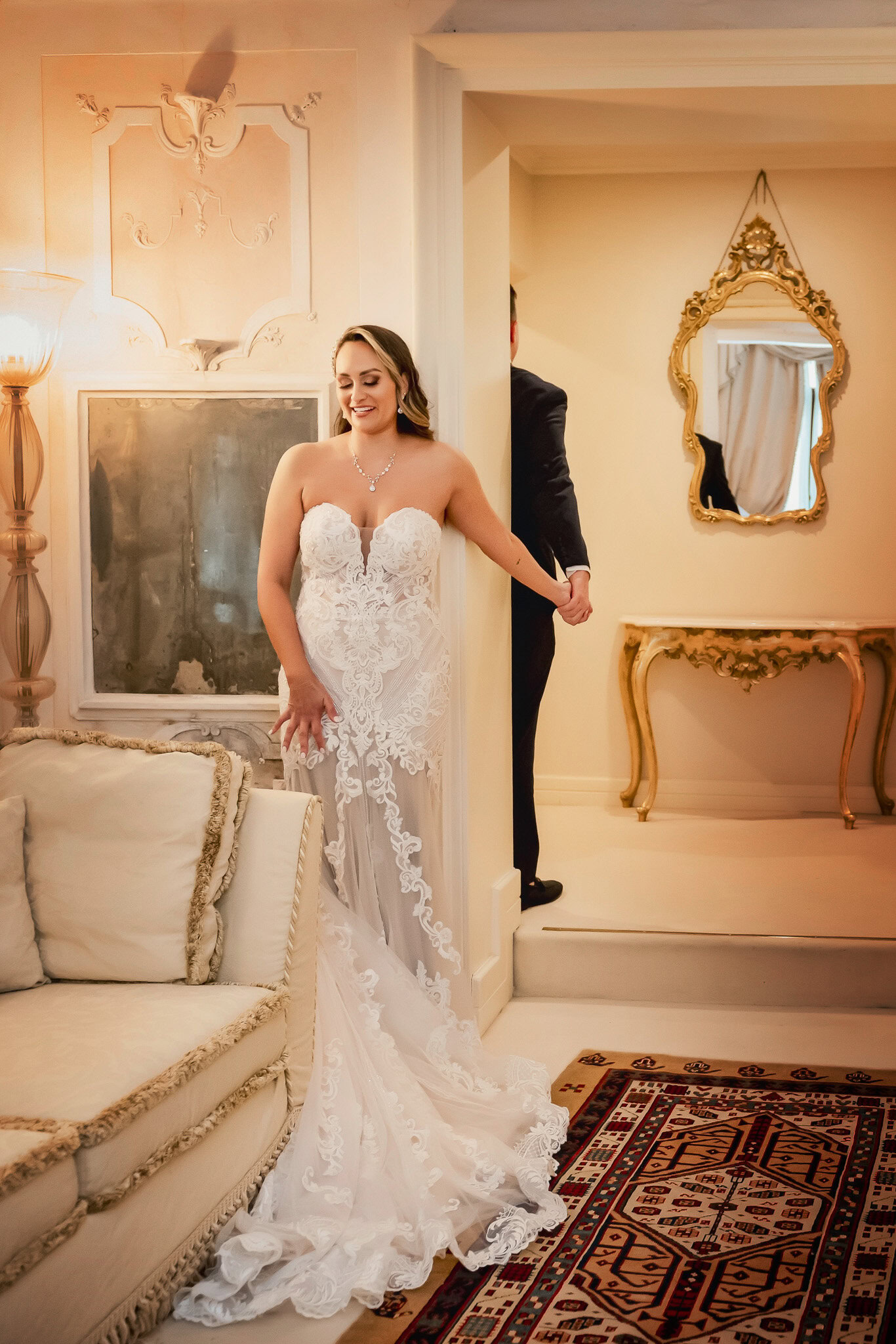 Elegant bride in a lace wedding gown holding hands with her groom in a Venetian palace int.