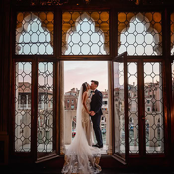 Bride and groom kissing inside a Venetian palace with stained glass windows.