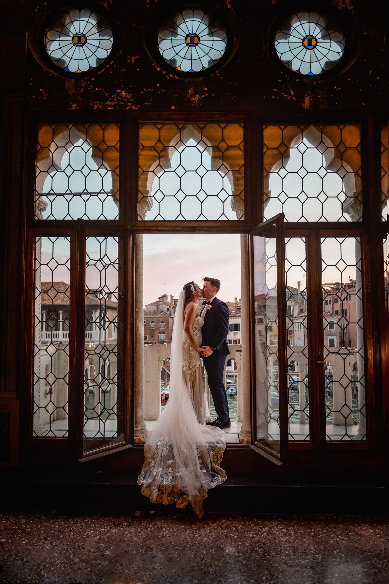 Bride and groom kissing inside a Venetian palace with stained glass windows.