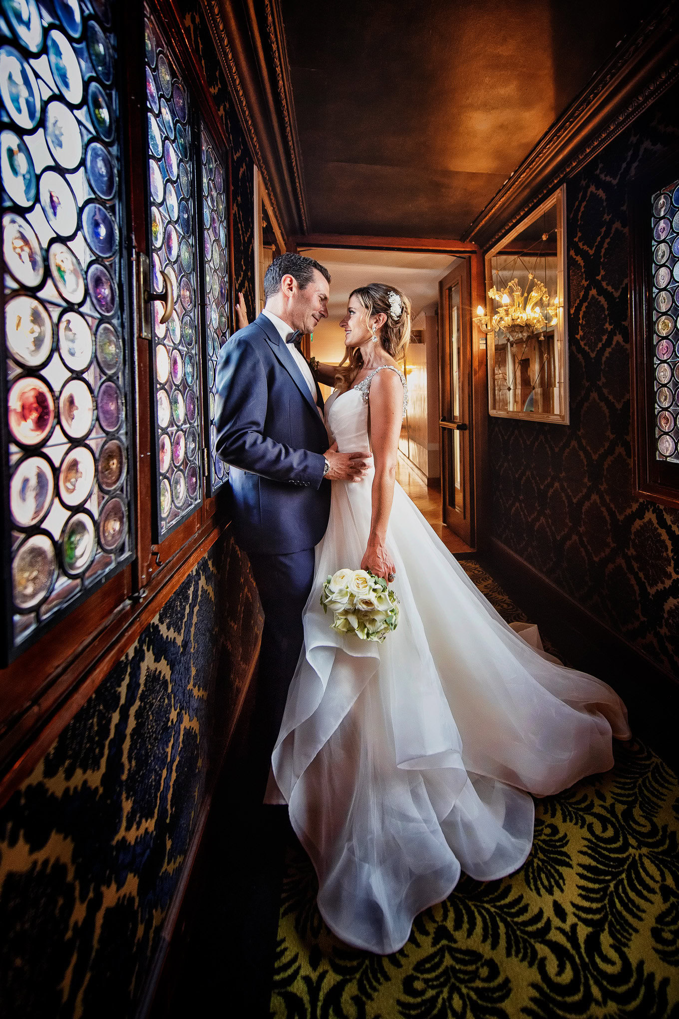 Intimate couple sharing a tender moment in a richly decorated Venetian interior with colorful stained glass windows.