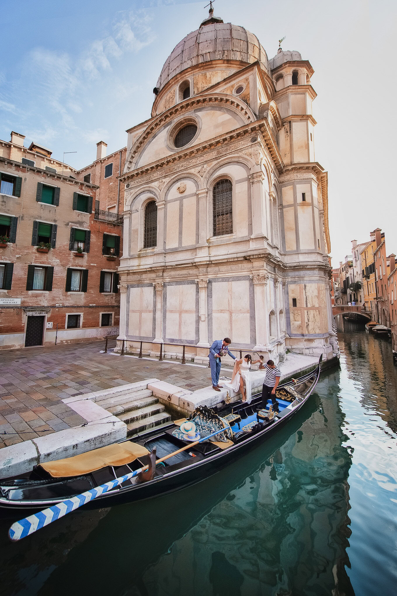 A woman and a gondolier preparing a gondola near a historic Venetian church on a sunny day.
