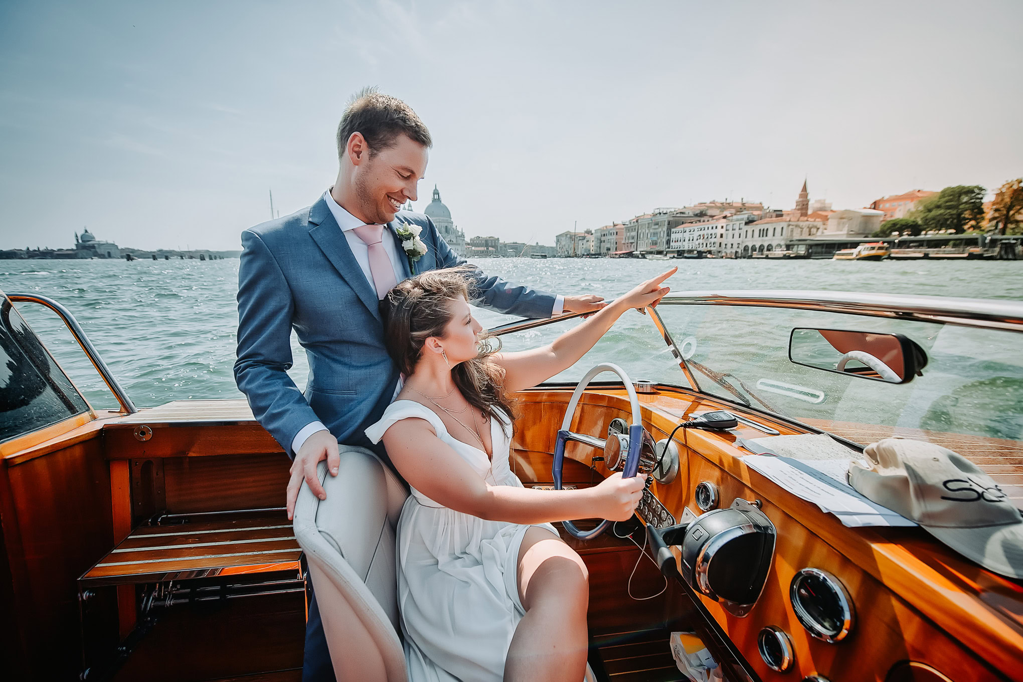 Intimate couple sharing a joyful moment on a boat along the Venetian canal with historic cityscape in the background.