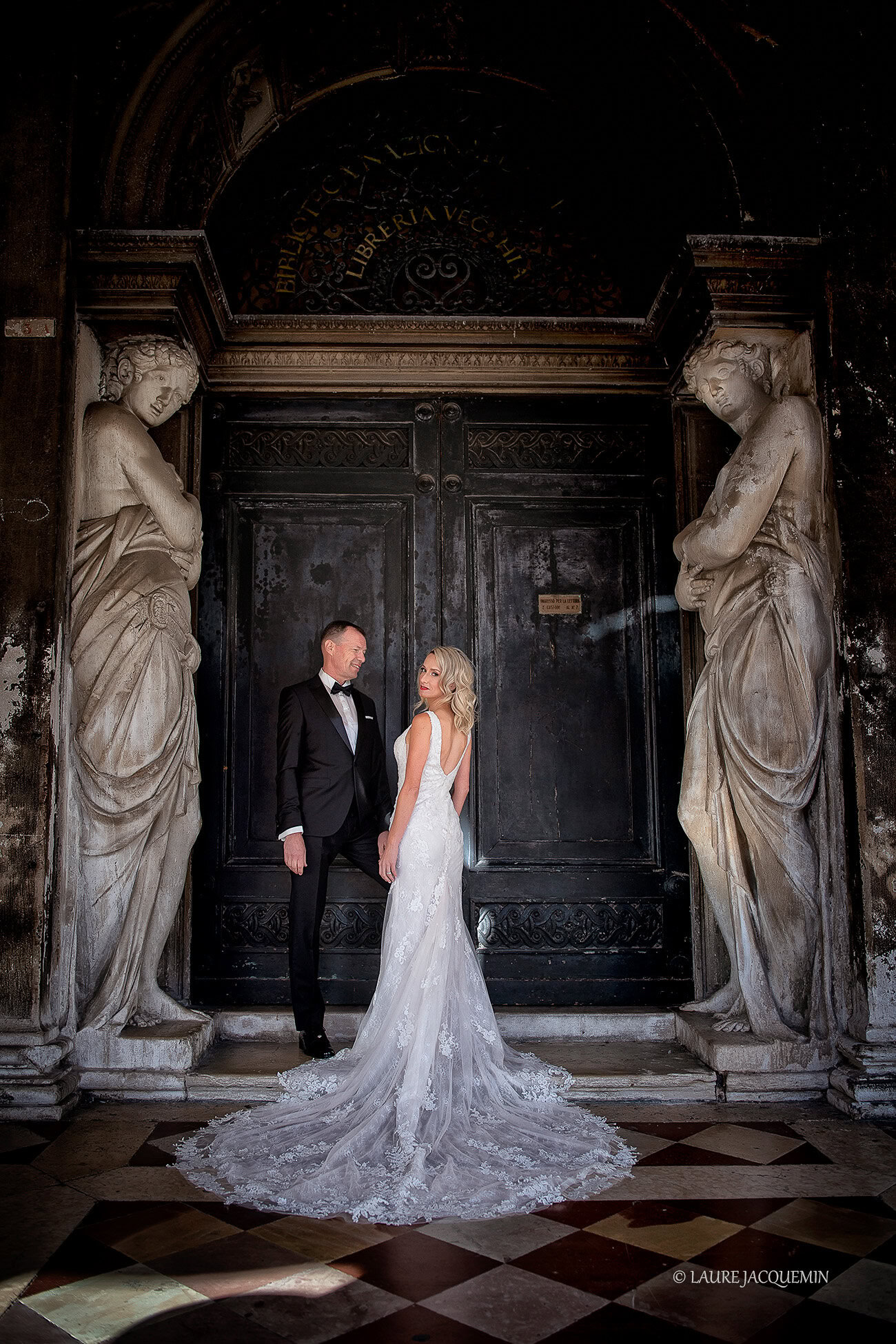 Intimate couple sharing a tender moment beneath grand Venetian architecture with soft, natural light.