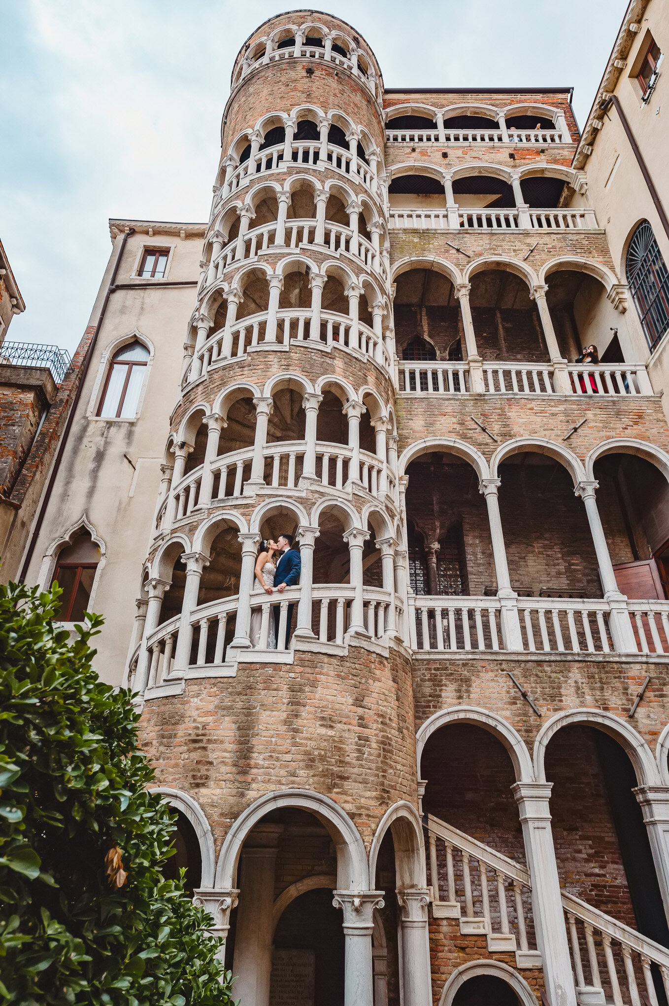 A couple sharing an intimate moment on a balcony of a historic Venetian building with ornate architecture.