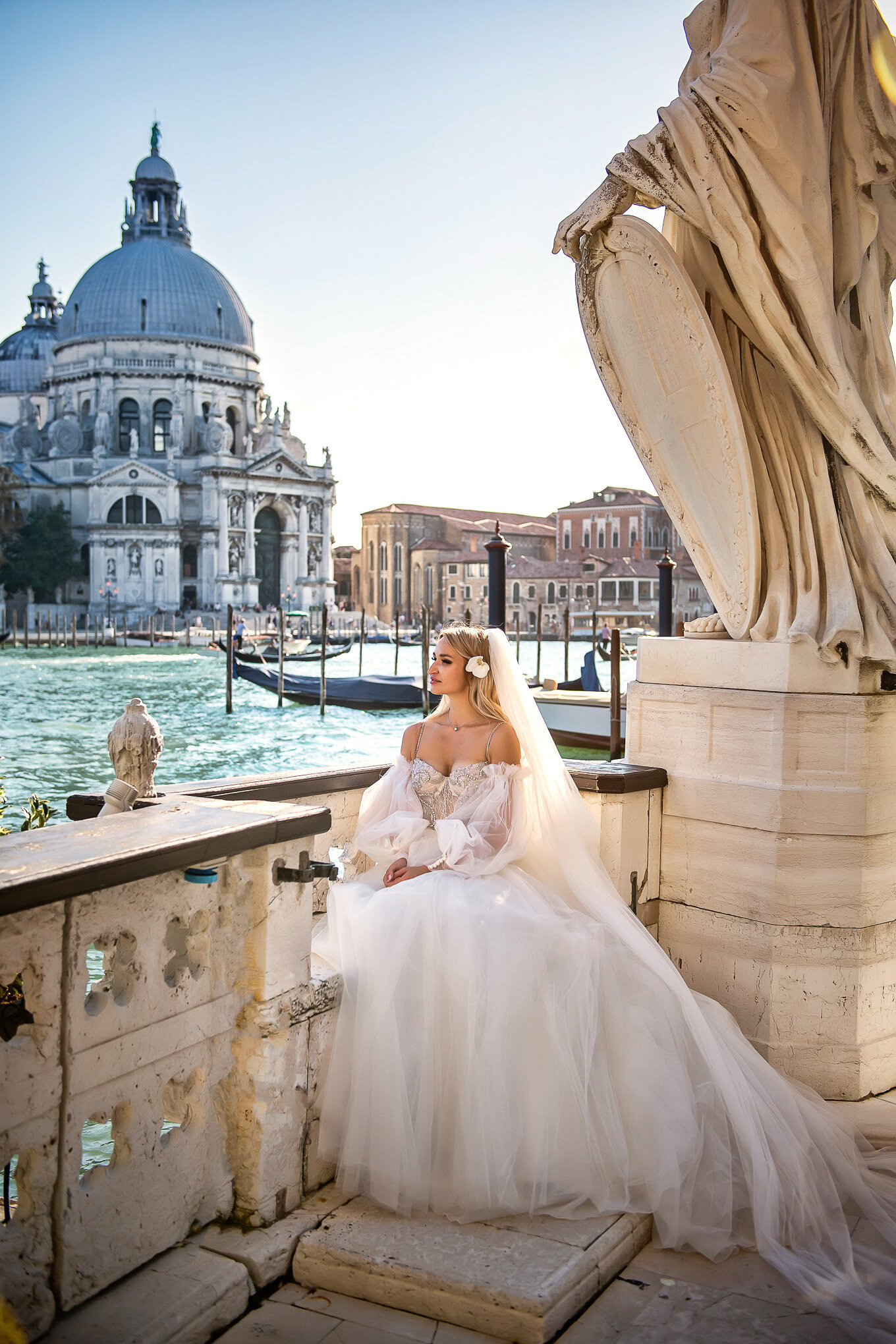 Intimate couple seated by Venice canal, soft sunlight highlighting romantic atmosphere and historic architecture.