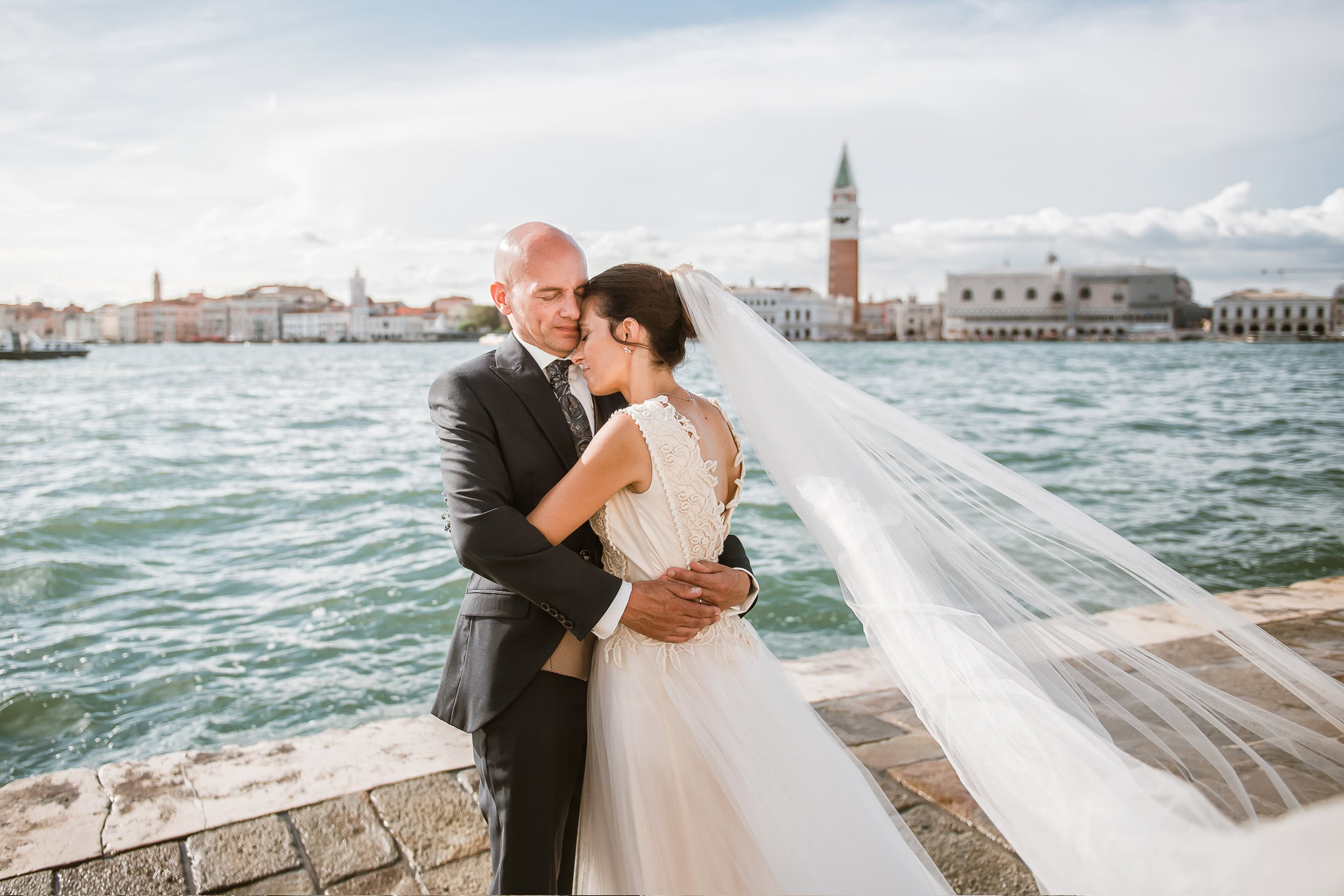 A couple shares an intimate moment by the Venetian waterfront, bathed in soft natural light, with historic cityscape and.