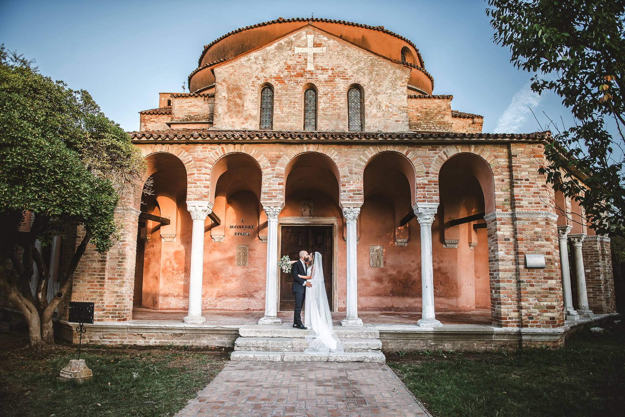 A couple shares a tender moment in front of a historic Venetian church bathed in warm evening light.