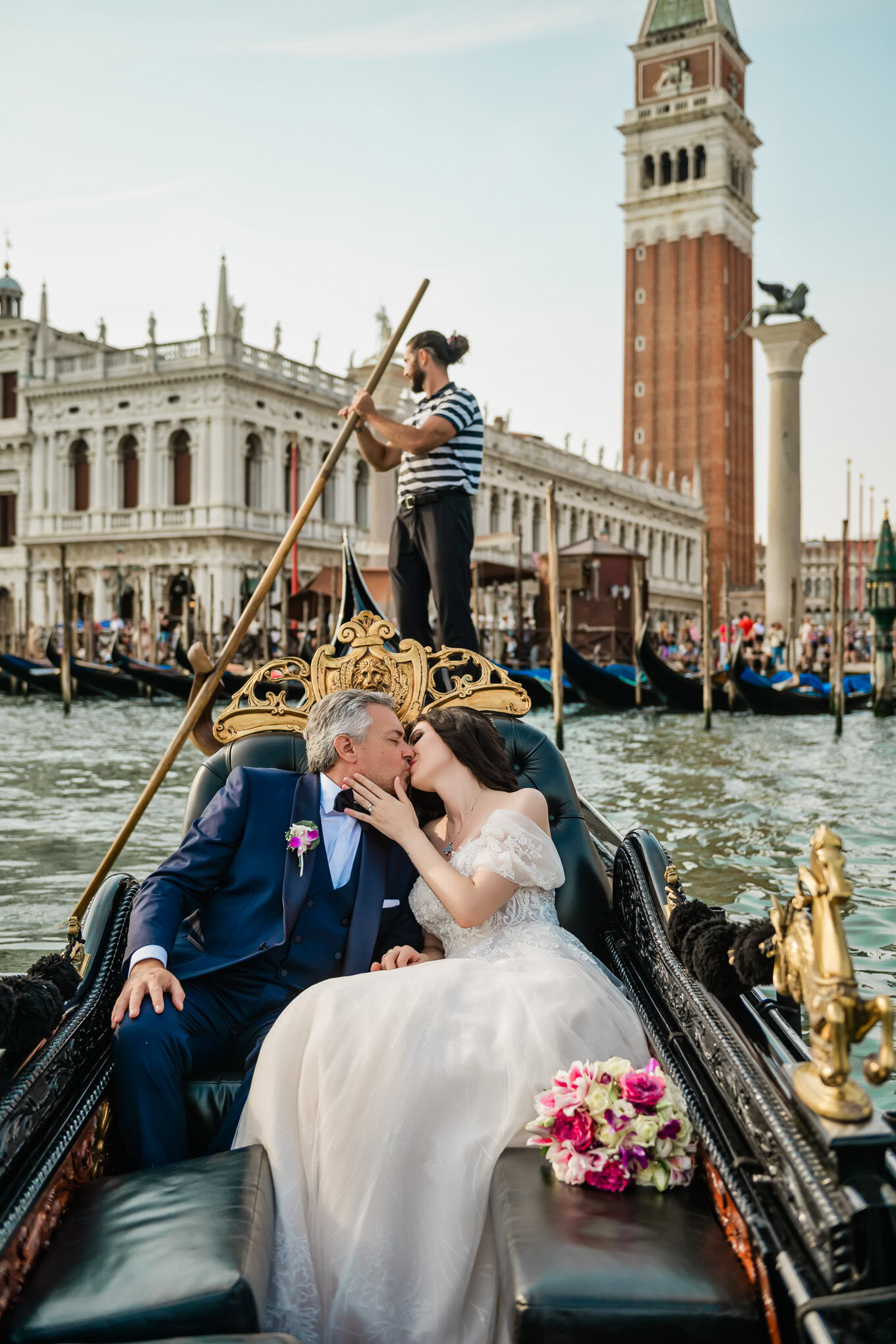 A couple sharing an intimate moment on a gondola in Venice, with historic architecture and a gondolier in the background.