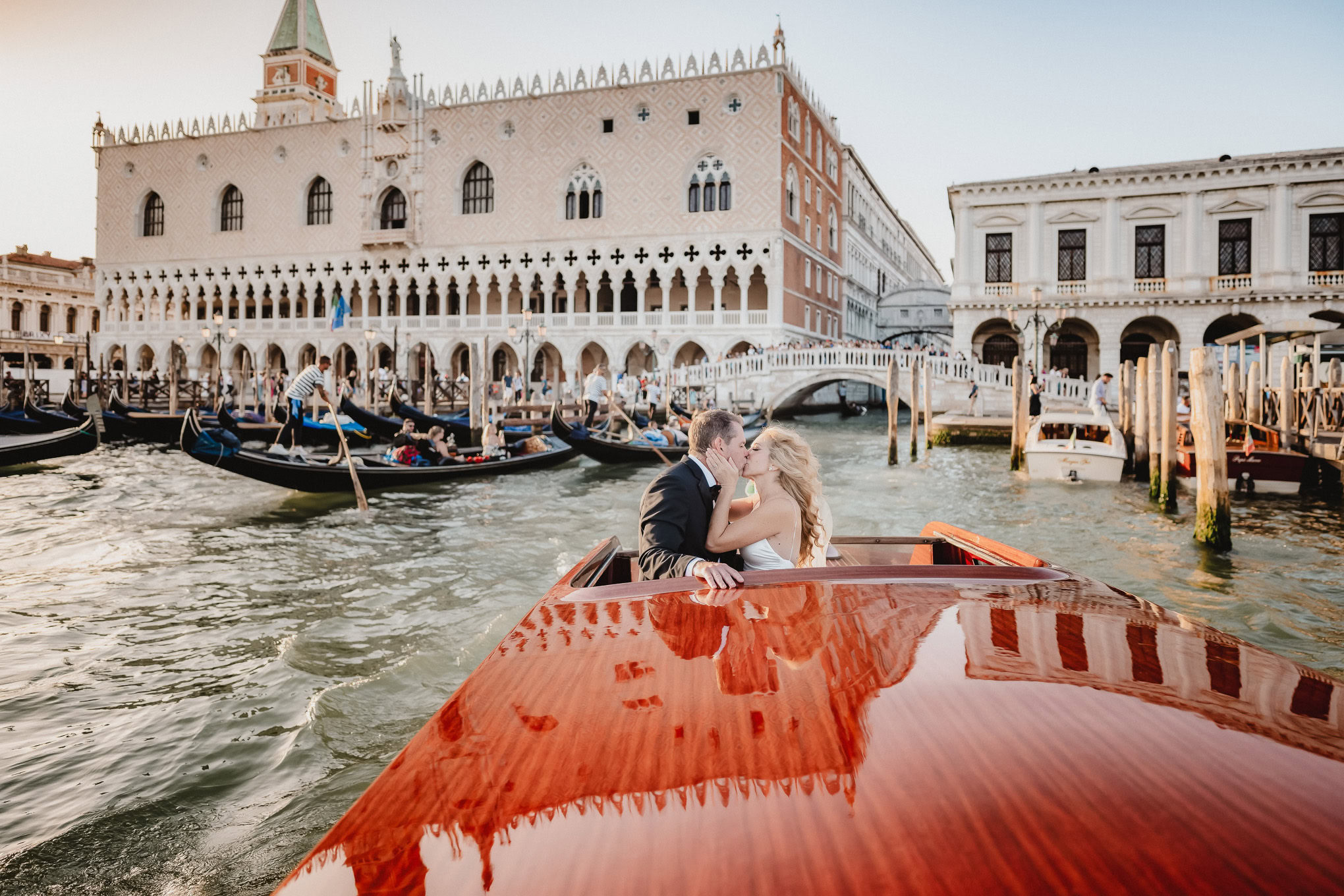 A couple sharing an intimate moment on a gondola in Venice, illuminated by soft natural light, with historic architecture.